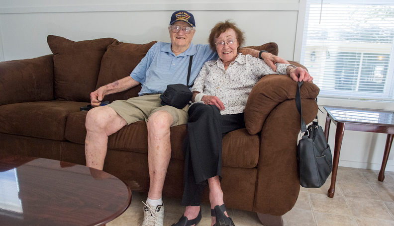 Flood survivors Clyde R. Meyers and his wife, Jean, smile as they relax for the first time on the sofa inside of the Manufactured Housing Unit (MHU) installed on their property in Denham Springs, La. Through the window in the background is a glimpse of the house they've lived in since 1961 that was damaged by 2016 historic flooding in Louisiana. (Photo by J.T. Blatty/FEMA)