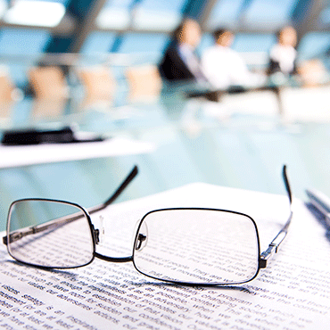 reading glasses on a document in foreground with out-of-focus people in background